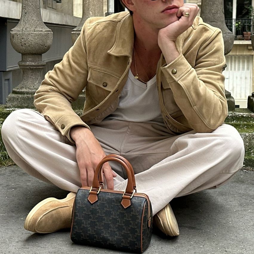 A man in beige slacks and a beige jacket with a Celine Triomphe Canvas Calfskin Small Boston Bag in Tan