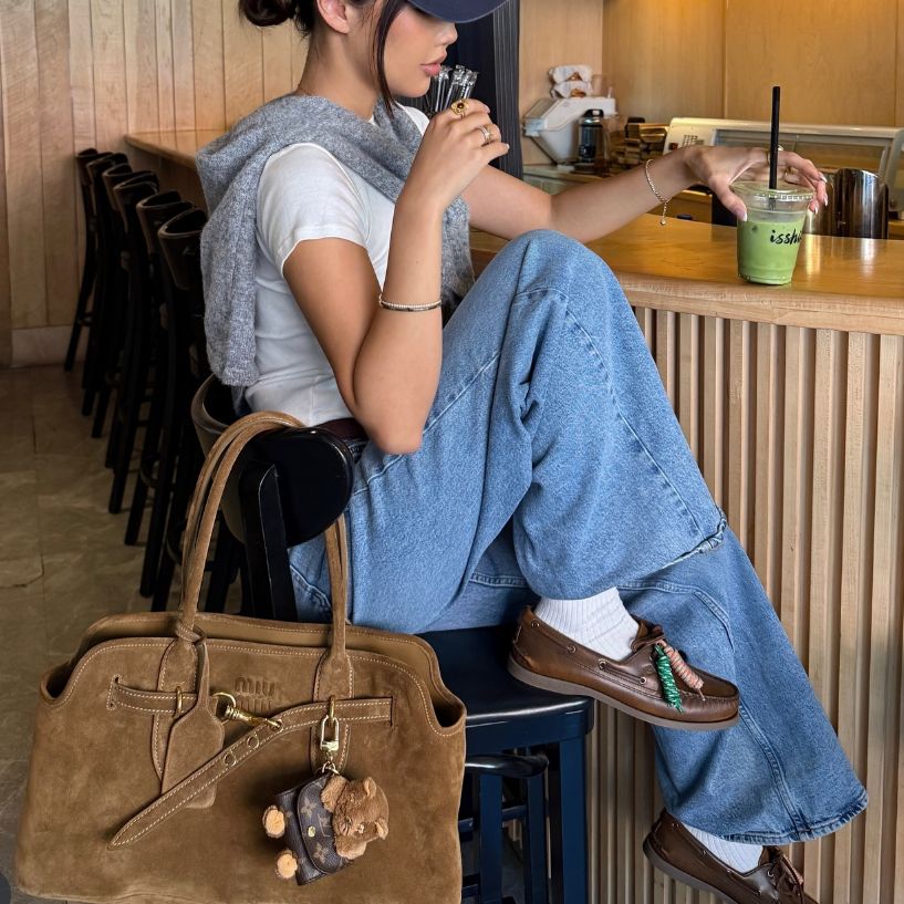 a woman in denim pants and a white t shirt with a grey sweater around her shoulders with a brown Miu Miu Aventure Bag