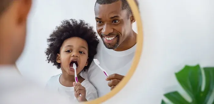 Criança escovando os dentes com o pai 