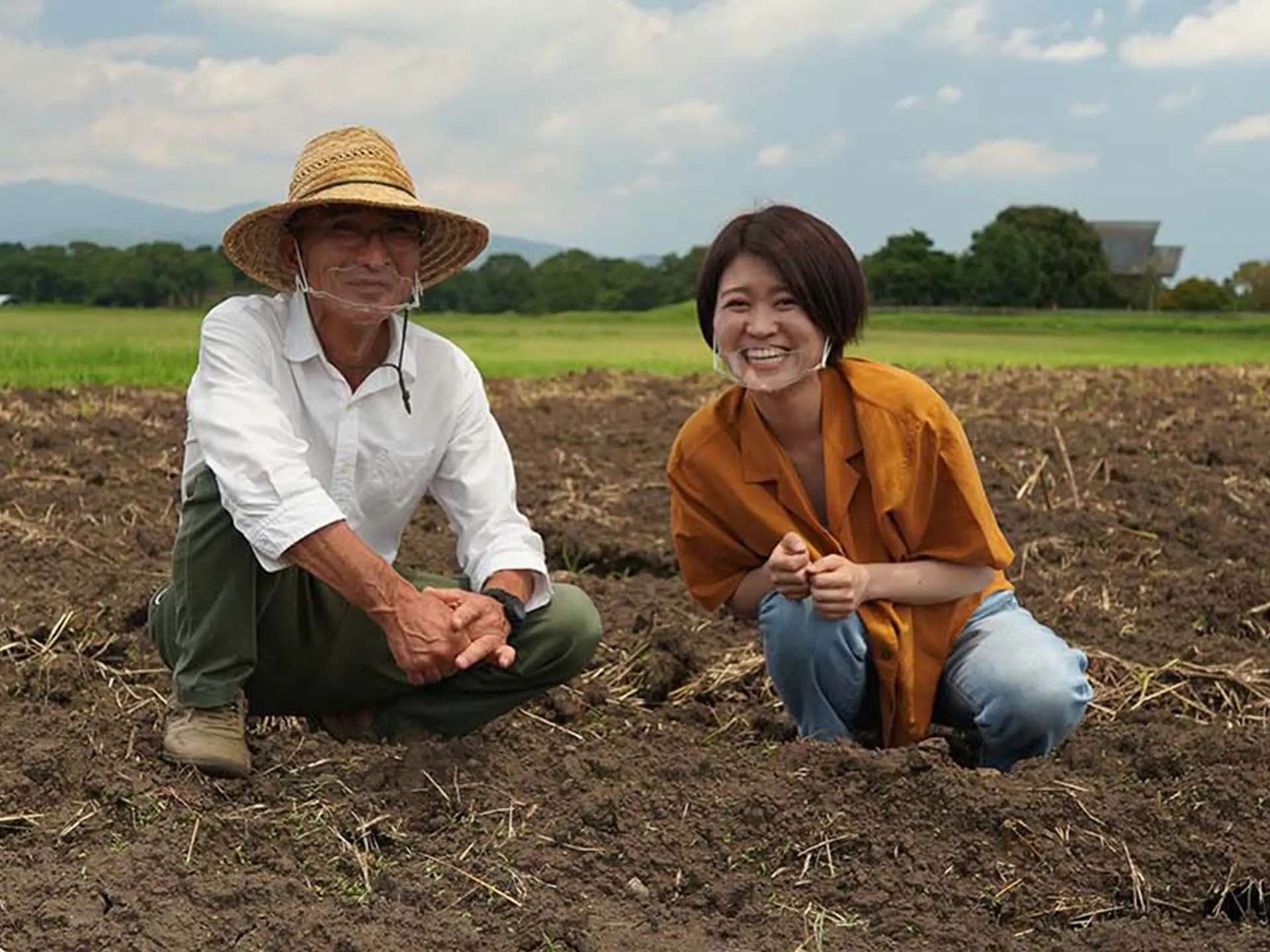 Yui Ogata accroupie dans un champ avec une autre femme