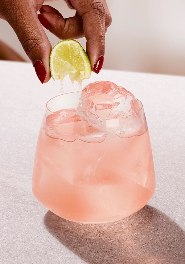 Sea Breeze con Ketel One en un vaso con hielo y una mano añadiendo spritz de lima