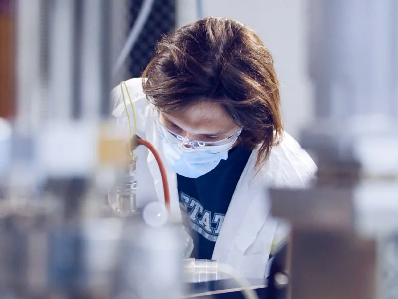 Masked student in white coat in research lab