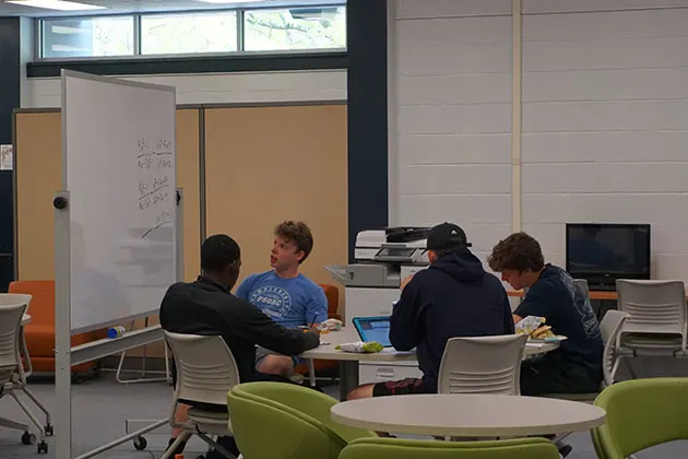 Photo of students working together around a table and using a marker board