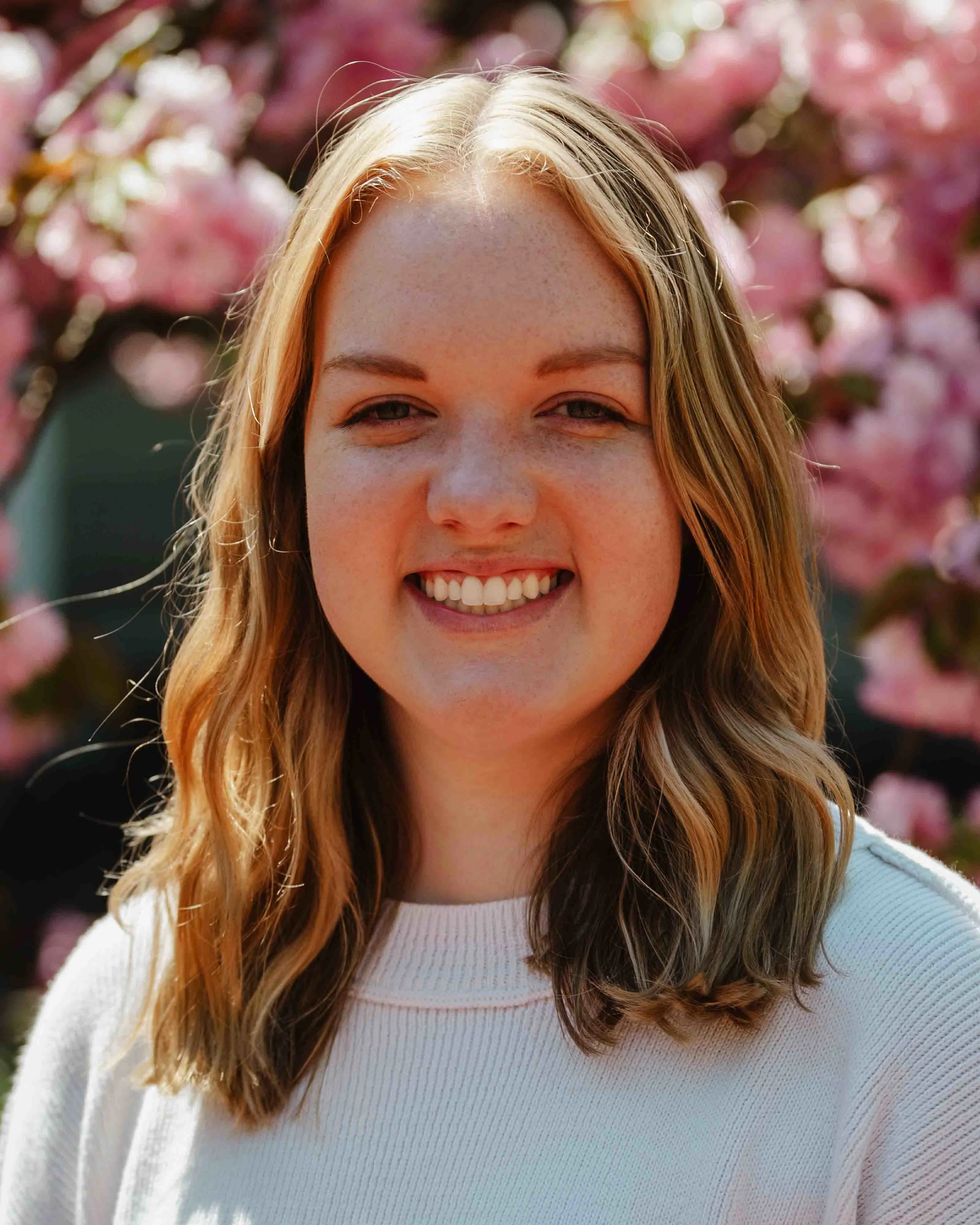 Courtney headshot outside wearing sweater with floral background