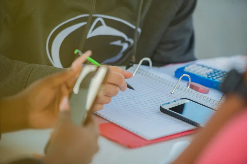 Notebook with a student taking notes. There is also a calculator and phone. 