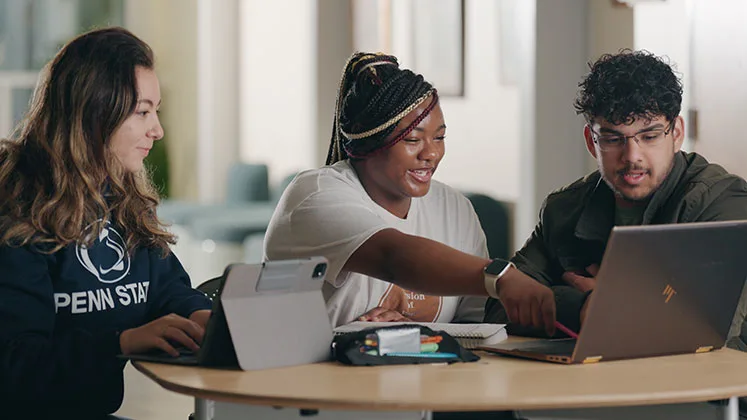 Photo of students sitting at a table and working together on a laptop