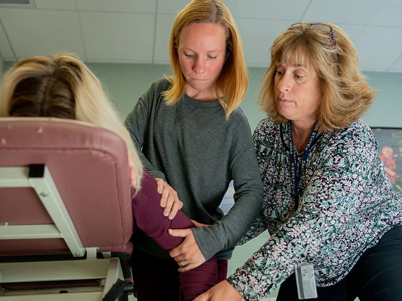 Instructor and student working together on stretching a classmate's shoulder. 