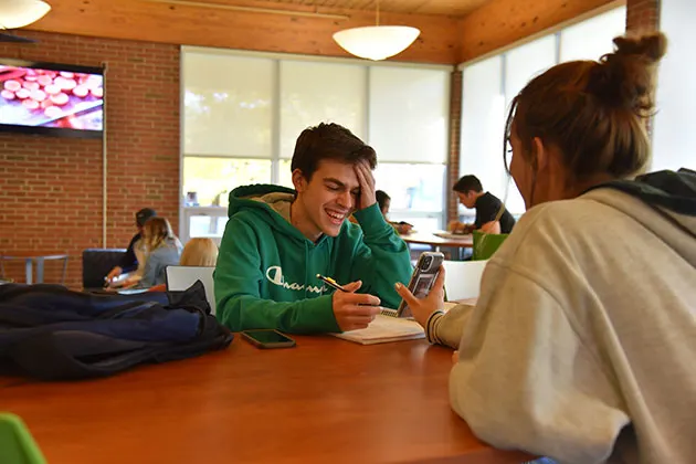Photo of students sitting and talking at a table in a lounge