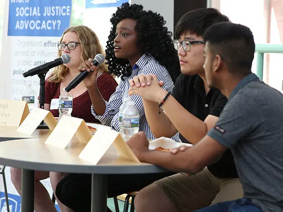 Photo of students sitting at a table with microphones and presenting to a group