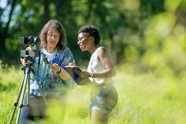 Photo of a student and instructor in a field with a camera, tripod, and clipboard