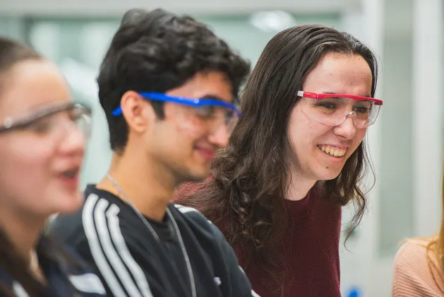 Photo of three students in a classroom wearing safety glasses