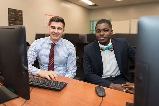 Photo of two students in ties sitting in a computer lab