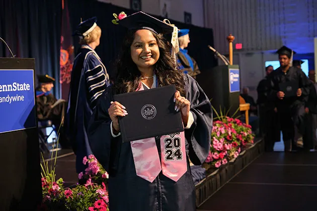 Photo of a student in their cap and gown holding a diploma at commencement