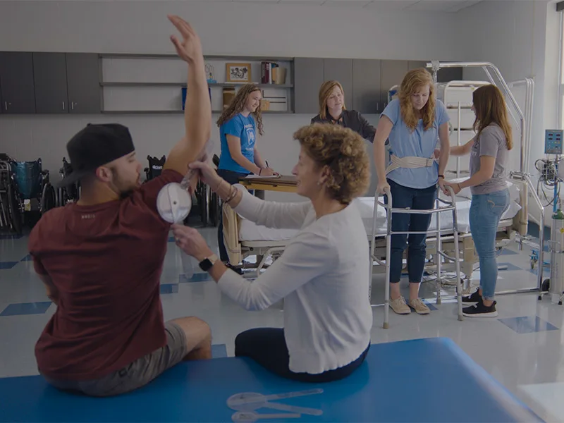 A classroom of occupational therapy students testing flexibility and using adaptive devices.