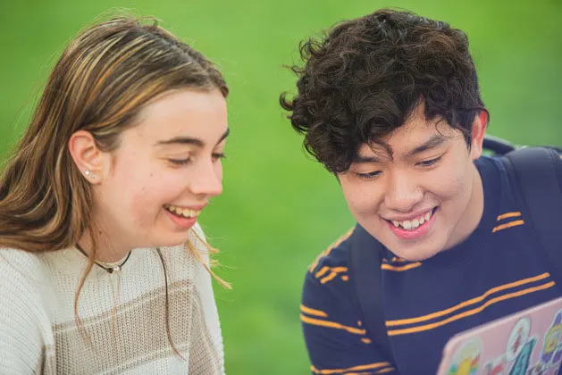 Two students laughing while looking at a laptop screen