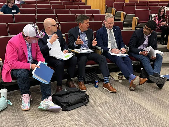 five people serving as case competition judges sit in auditorium seats talking