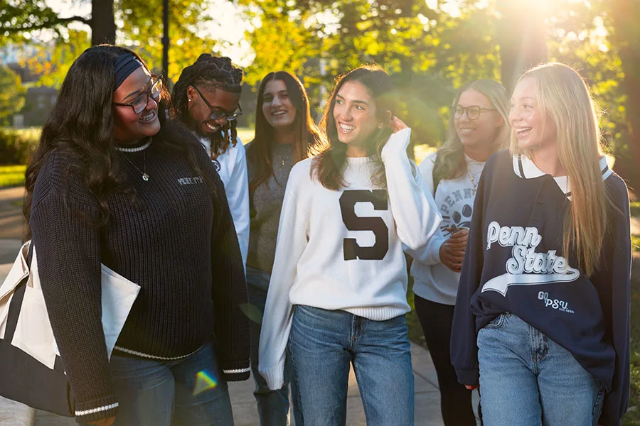Gathering of Penn State Students laughing together on a sunlit campus path. 