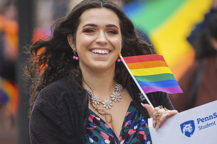 Smiling student holding a rainbow flag