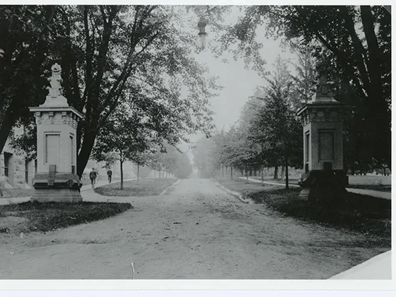 The entrance to Penn State's campus in the early 1900s. There is a pillar on either side of the road.