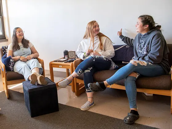 Three students talking in an apartment living room.