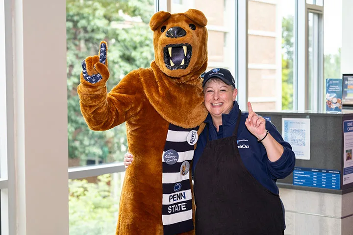 A Penn State staff member poses with the Nittany Lion mascot, both are holding up the number one with their hands.