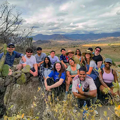 Photo of a group of study abroad students sitting together on a hill with mountains in the background