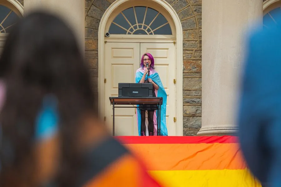 Student draped in Pride flag standing at podium speaking to audience