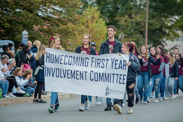 Students walking in homecoming parade holding a banner that says homecoming first year involvement committee
