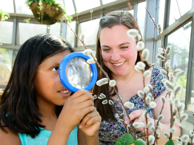 Student helping a child look at a plant with a magnifying glass.