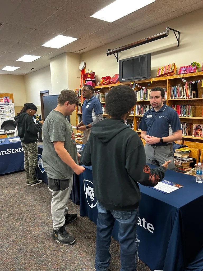 students speaking with Penn State staff at tabling event in library