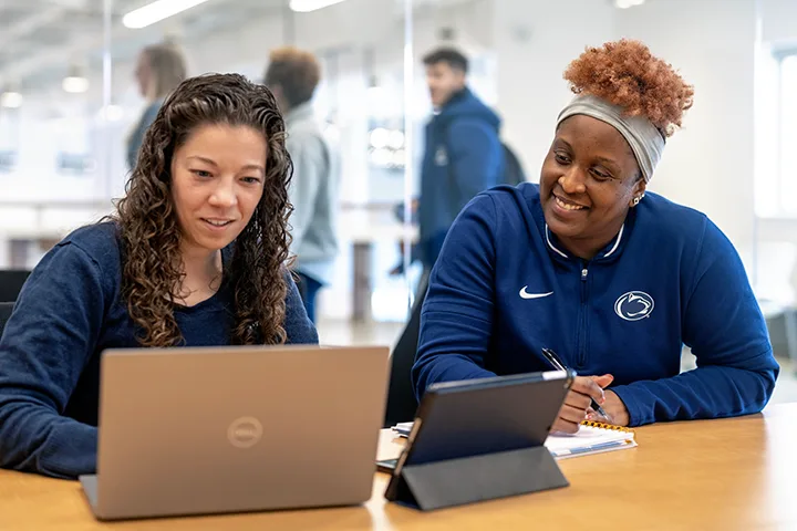 Penn State students in computer lab looking at laptop and laughing with each other. 