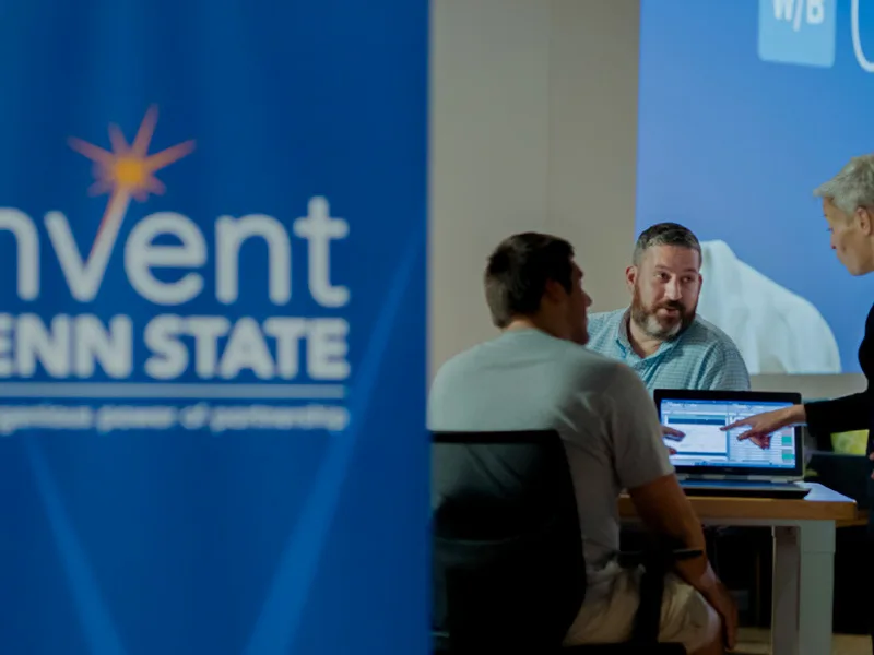 three people at a laptop with an invent penn state banner in foreground