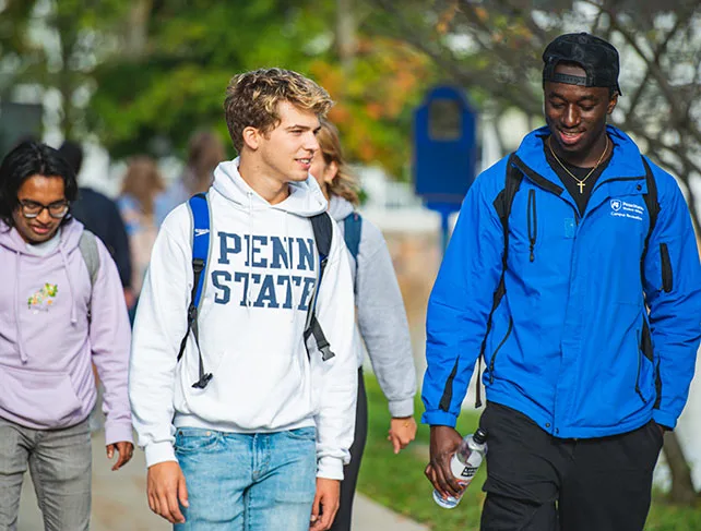 Penn State students having a conversation while strolling through campus on a sunny day.
