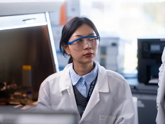 Photo of a student in a lab coat and protective eyewear sitting in a lab