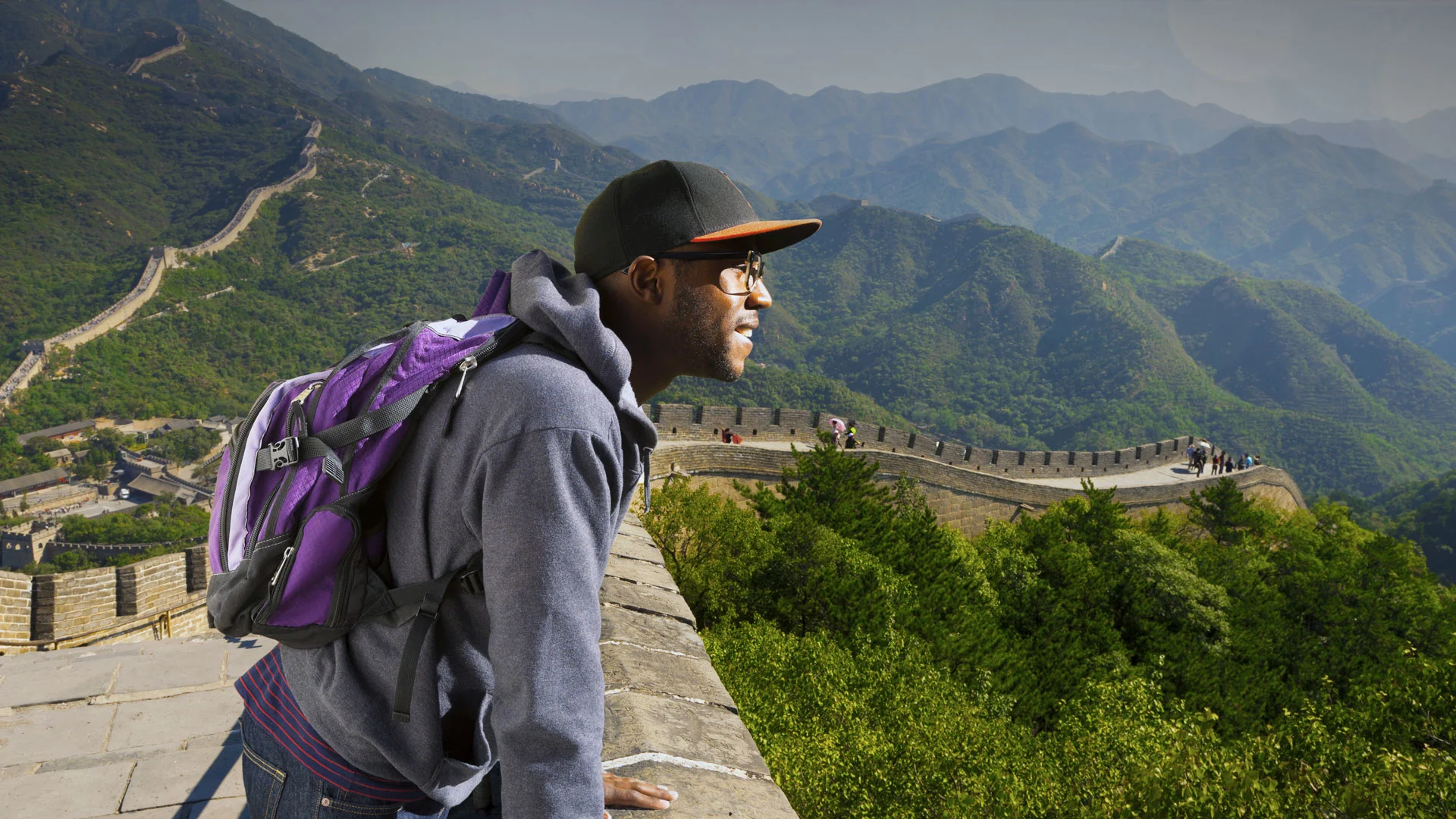 student in a ballcap and backpack standing on the Great Wall of China