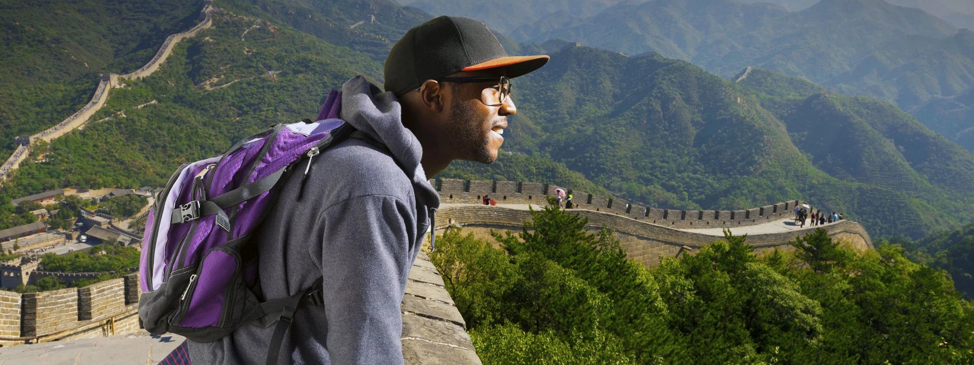 student in a ballcap and backpack standing on the Great Wall of China