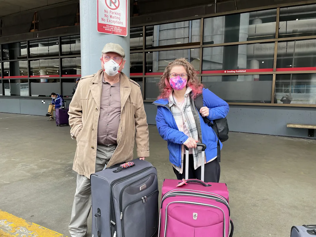 Two people with luggage smiling outside of an airport terminal