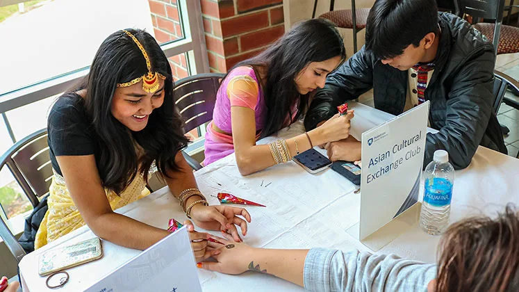Photo of students in the Asian Cultural Exchange Club applying henna at an involvement fair