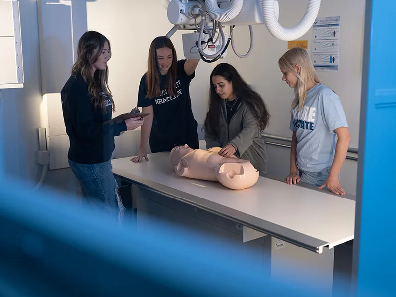 Four students placing a mannequin below an x-ray arm.