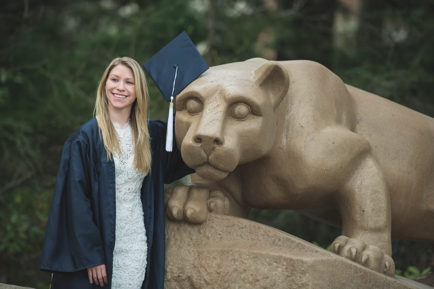Student in cap and gown standing with Lion Statue.