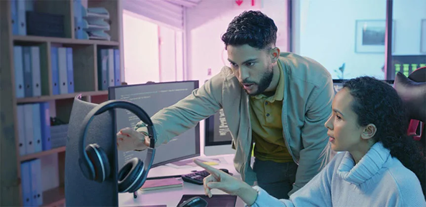 Photo of two students talking and pointing at code on a computer