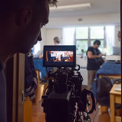 A cameraperson filming a scene, looking at the video screen