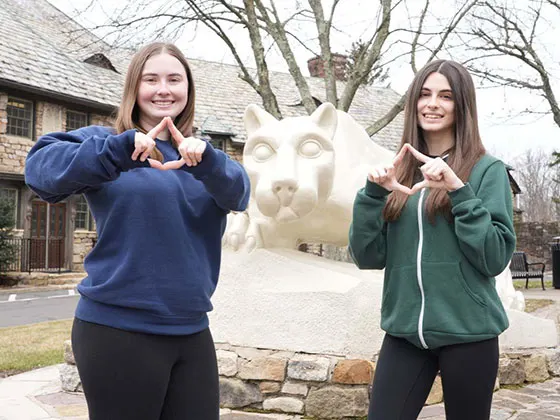 Photo of two students in front of Hazleton's lion shrine making a diamond with their hands
