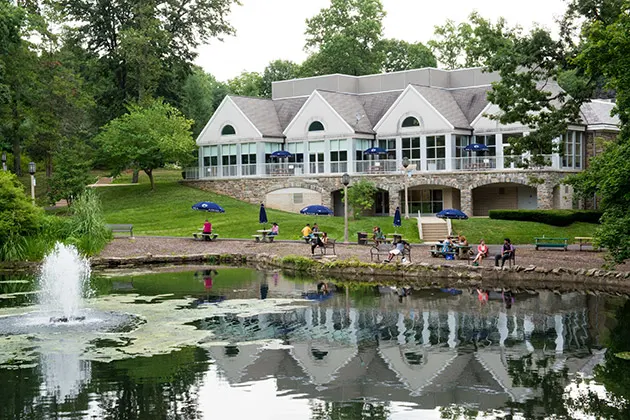 Photo of students sitting at tables around a pond in front of a large building