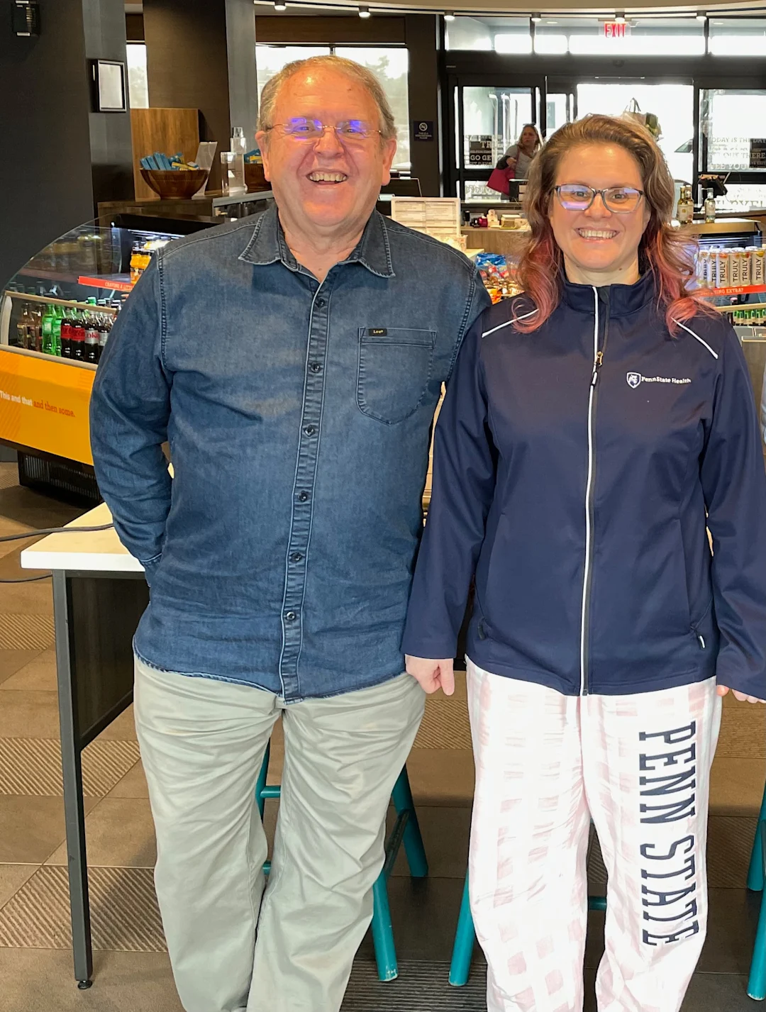 Two people standing in a hospital cafe, smiling at the camera