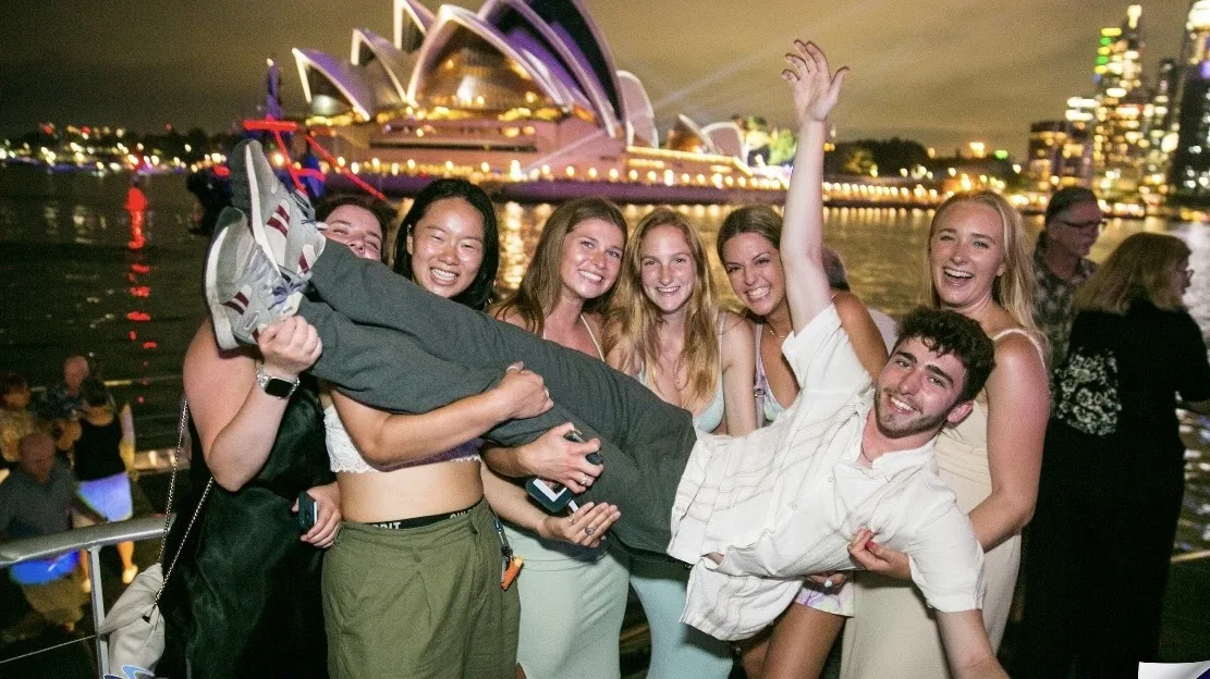 A group of students holding one student in front of the Sydney Opera House