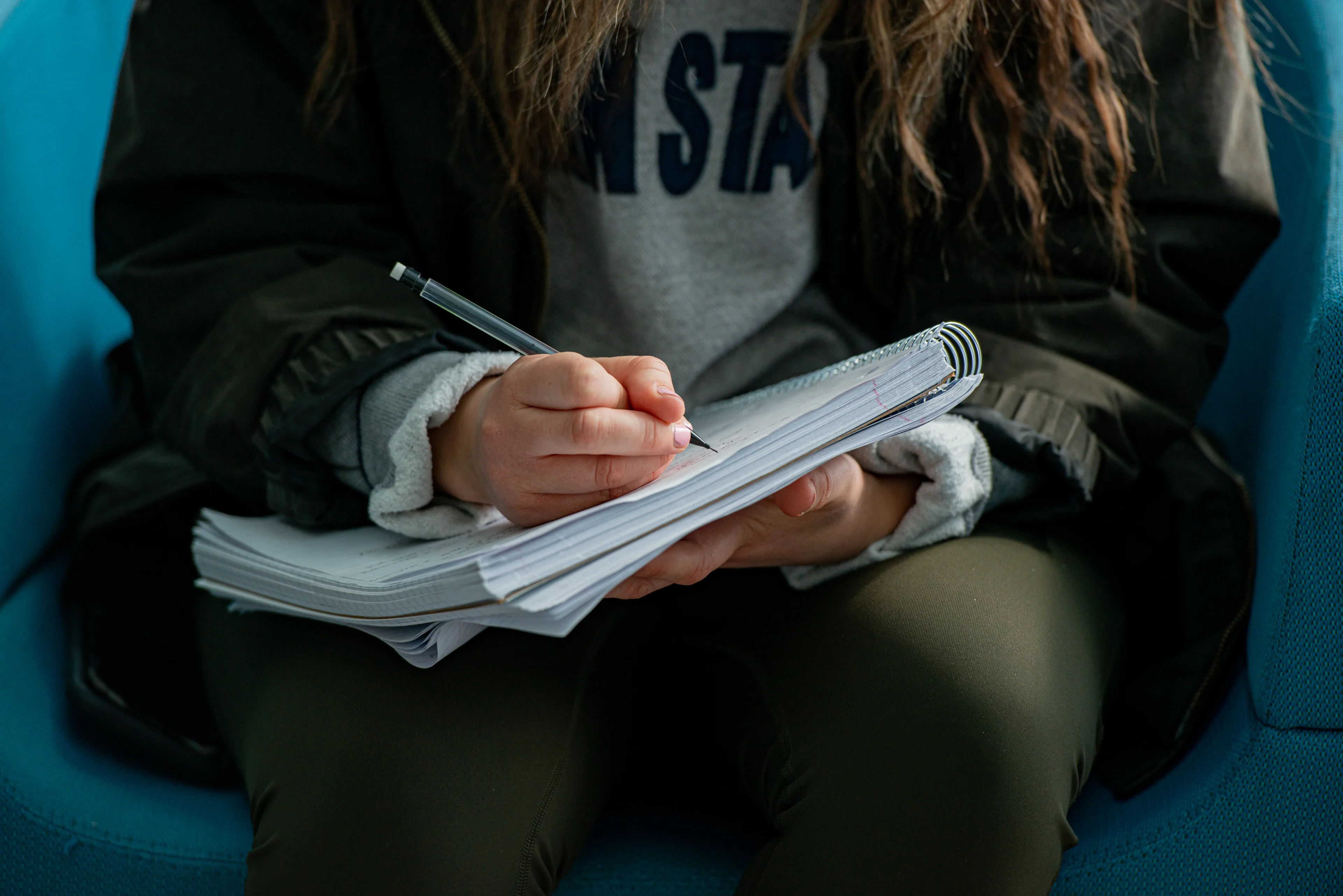 Student with Penn State sweatshirt writing in notebook.