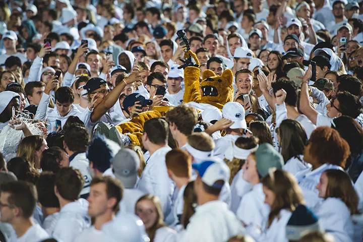 The Penn State mascot crowd surfing in a group of people wearing white and blue clothing.