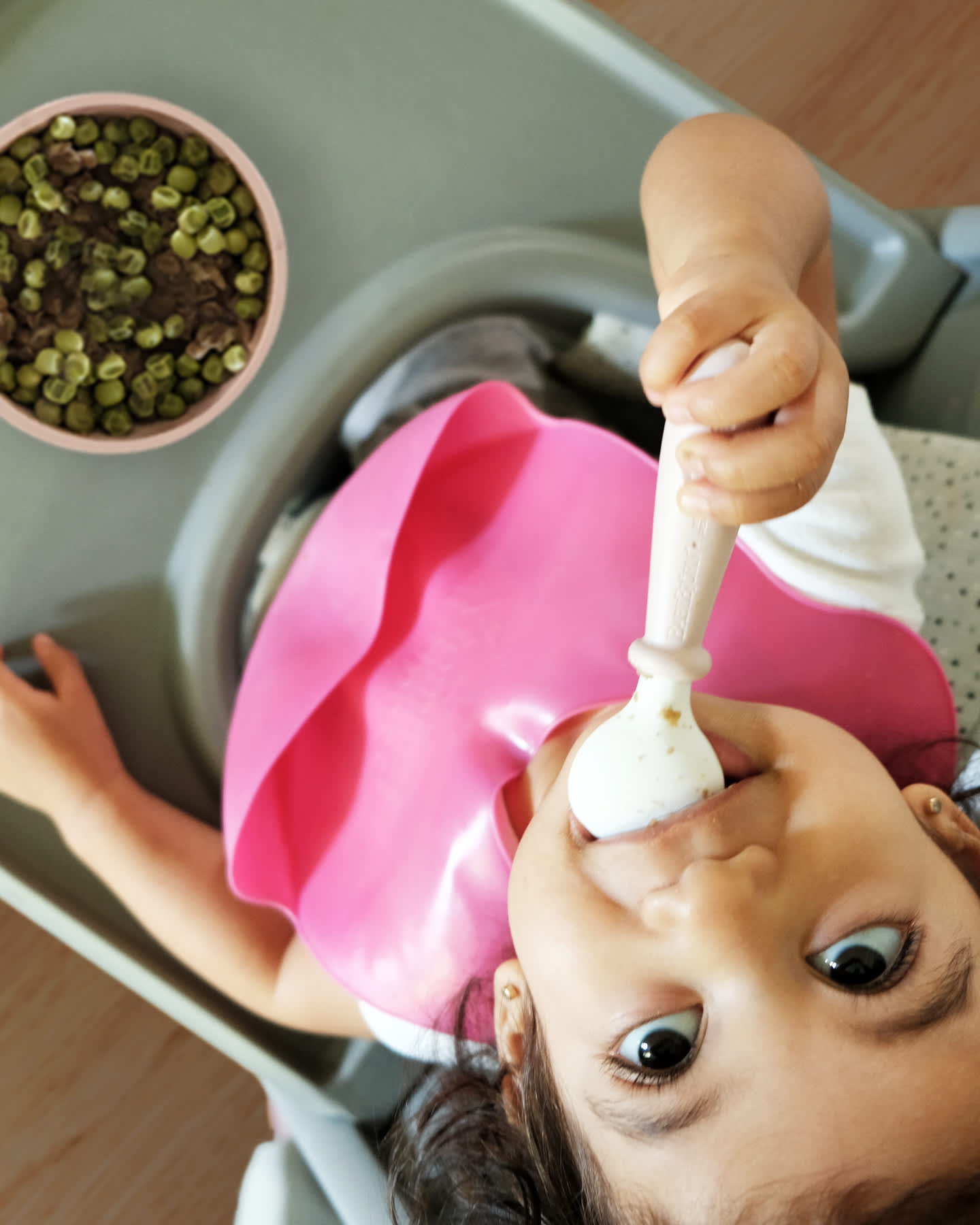 Toddler eating peas in a bowl