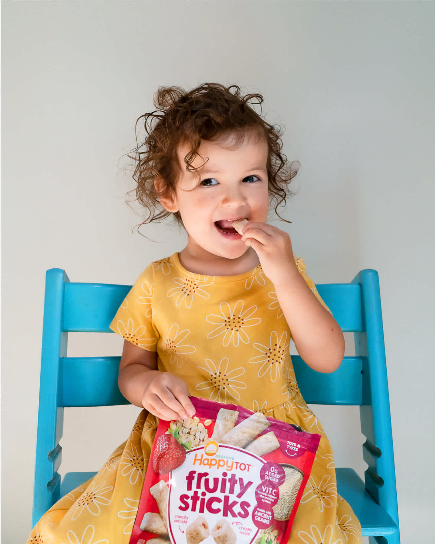 smiling girl sitting on blue chair and eating strawberry fruity sticks